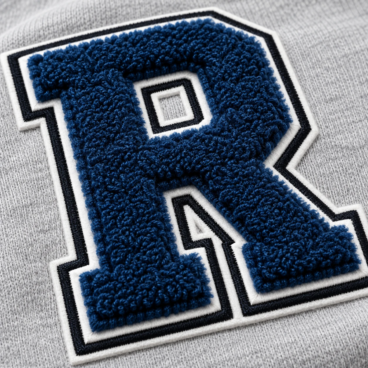 Blue letter R chenille patch on gray fabric